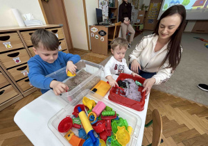 Chłopcy bawią się autkami w piasku kinetycznym.
