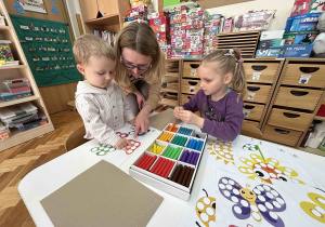 Dziewczynka z 6 latków pomaga chłopcu w wyklejaniu plasteliną.