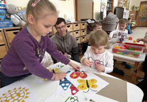 Dziewczynka z 6 latków pomaga chłopcu w wyklejaniu plasteliną.