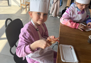 Dziewczynka trzyma kawałek pizzy.