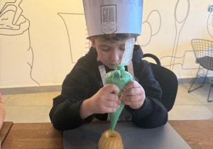 Chłopczyk nakłada lukier na babeczkę.