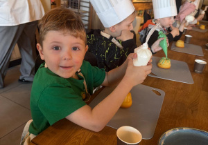 Chłopczyk nakłada lukier na babeczkę.