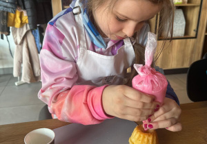 Dziewczynka przyozdabia babeczkę lukrem.