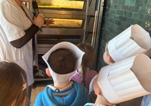 Pani pokazuje dzieciom piec do wypiekania słodkości i bułeczek.