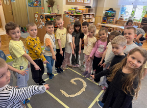 Dzieci stoją w kole i wskazują literę g.