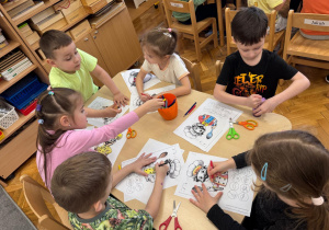 Dzieci siedzą przy stoliku i wykonują pracę plastyczną.