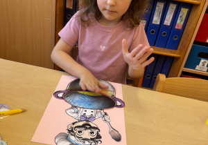 Dziewczynka przykleja garnek na swojej pracy.