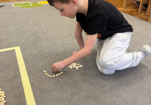 Chłopiec układa literę g z ziaren grochu.