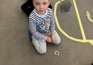 Chłopiec siedzi na dywanie z ułożoną literą g z grochu.