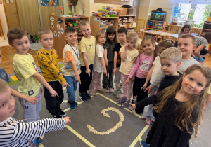 Dzieci wskazują na literę g ułożoną z ziaren grochu.