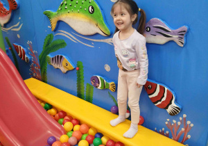 Dziewczynka skacze do basenu z kulkami.