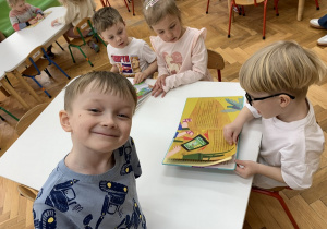 Dzieci przy stoliku oglądają kolorowe ilustracje.