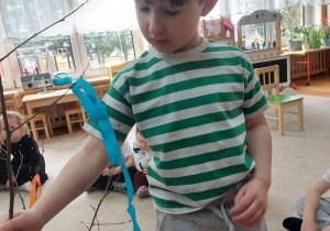 Chłopiec obwiązuje gałązkę bibułą.