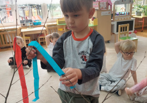 Chłopiec przywiązuje paski bibuły do gałązki.