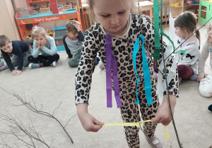 Dziewczynka przywiązuje do gałązki żółty pasek bibuły.