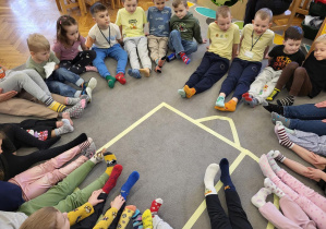 Dzieci siedząc witają się skarpetkami.