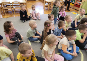 Dzieci siedzą na dywanie i opowiadają o swoich spostrzeżeniach.