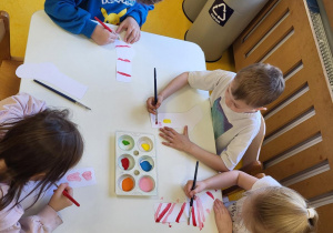 Dzieci siedzą przy stoliku i ozdabiają skarpetki.
