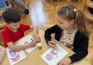Dzieci siedzą przy stoliku i kolorują Tremka.