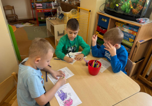 Chłopcy kolorują swoją pracę kredkami.