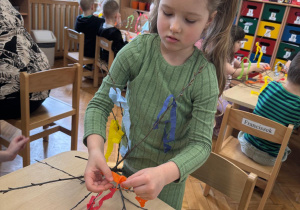 Dziewczynka ozdabia gałązkę kolorową bibułą.