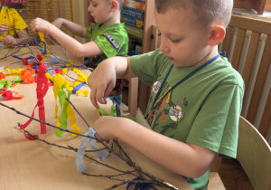 Chłopiec starannie ozdabia gałązki kolorową bibułą.