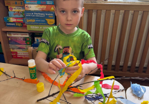 Chłopiec zawiązuje kolorowe wstążki bibuły na gałązce.