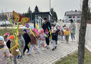 Uśmiechnięte przedszkolaki maszerują po chodniku.