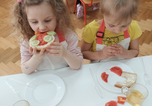 Dziewczynka je kanapkę z ogórkiem, papryką i pomidorem.