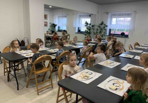 Dzieci siedzą przy stolikach.