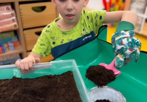 Chłopiec sypie ziemię.