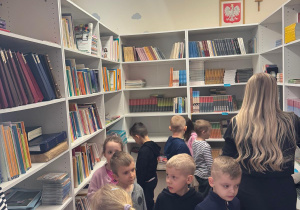 Dzieci oglądają książki zgromadzone w bibliotece.