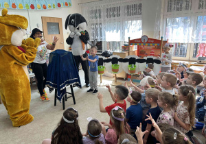 Dzieci siedząc na dywanie wyciągają ręce.