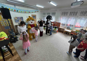 Panie i zające maskotki stoją, a dzieci wkładają jajka.