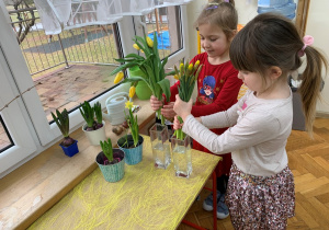 Dziewczynki układają kwiaty w wazonie.