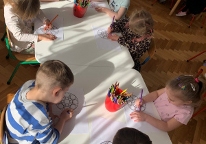 Dzieci kolorują kredkami mandalę.