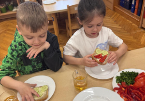 Chłopiec z dziewczynką spożywają przygotowane przez siebie kanapki.