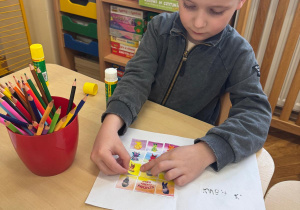 Chłopiec wkleja Pana Ble do swojej książeczki.