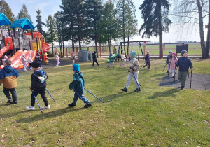 Dzieci maszerują z kijkami na placu zabaw.