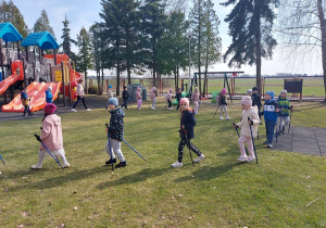 Dzieci maszerują z kijkami na placu zabaw.