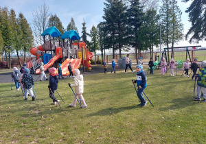 Dzieci maszerują z kijkami na placu zabaw.