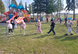 Dzieci maszerują z kijkami na placu zabaw.