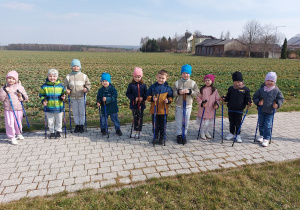 Przedszkolaki stoją w szeregu z kijkami.