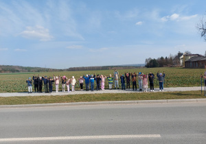Przedszkolaki stoją w szeregu i trzymają kijki do Nordic Walking w górze.