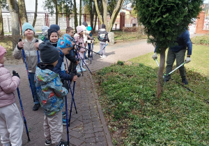 Dzieci podczas spaceru z kijkami obserwują wiosenne prace w ogrodzie.