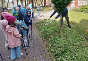 Dzieci podczas spaceru z kijkami obserwują wiosenne prace w ogrodzie.