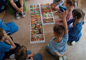 Dzieci siedzą na dywanie i przyglądają się obrazkom.