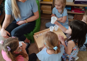 Dziewczynki trzymają kubeczki z różnymi przedmiotami.