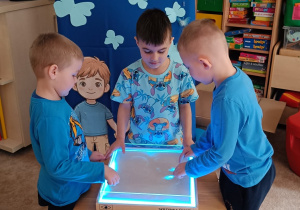 Chłopcy rysują palcami w kuwecie sensorycznej.