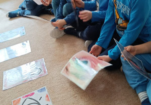 Dzieci trzymają w ręku ilustracje.